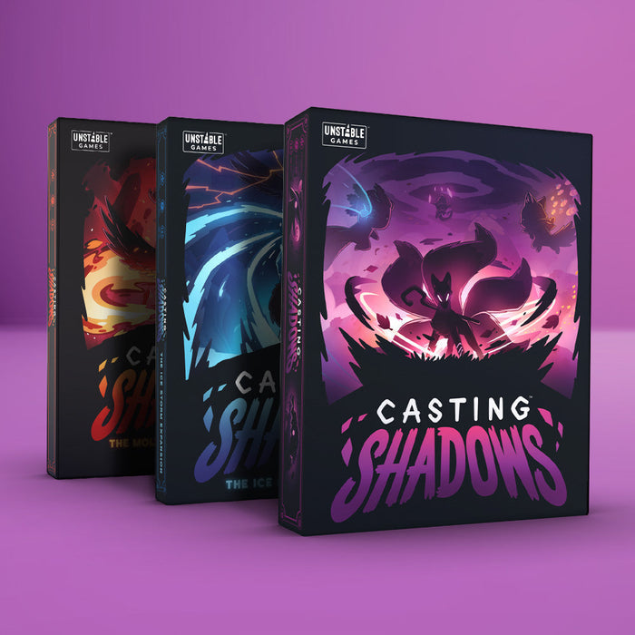 Three Unstable Games board boxes rest on a pink backdrop, with "Casting Shadows: Base Game + 2 Expansion Bundle" at the forefront. It showcases a dark mystical figure, ideal for strategic game fans and future Ultimate Shadow Casters.