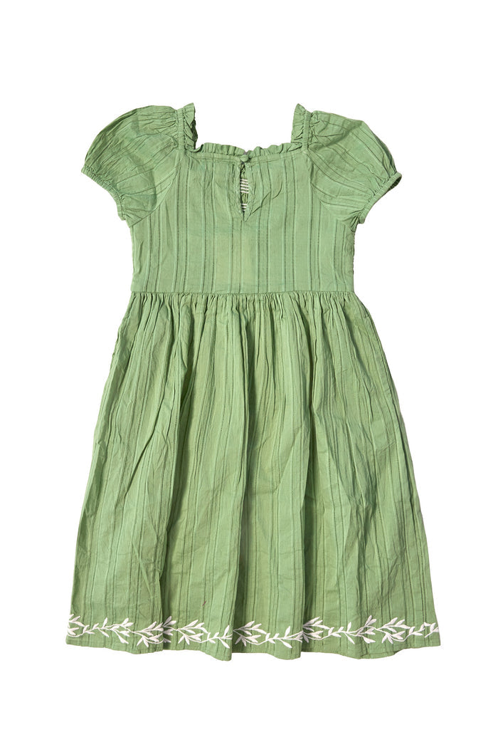 The Mini Journey Dress in Light Green by Ivy City Co is a girls’ cotton dress with a smocked bodice, short sleeves, knee-length cut, subtle vertical stripes, and white embroidered leaf details on the hem.