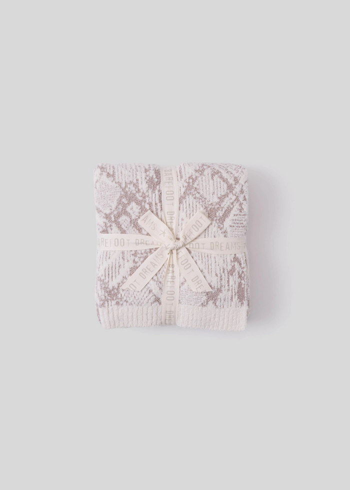 Cream and taupe blanket folded with a bow on a grey background