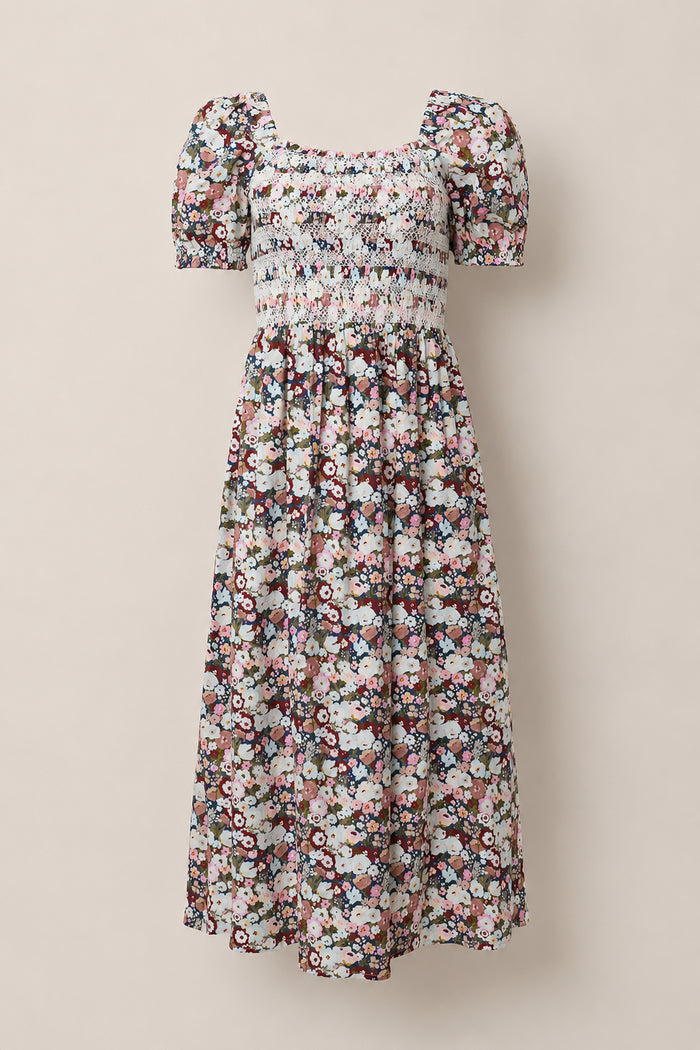 The Ivy City Co Sunday Best Dress in Midnight Garden features puff sleeves and an ankle-length silhouette with a smocked bodice, showcasing a multicolored floral pattern on a white background. Displayed against a neutral backdrop, this maternity-friendly style ensures effortless comfort and elegance.
