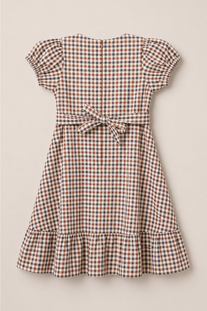 The Teen Connie Short Sleeve Dress in Chestnut Gingham by Ivy City Co is a short-sleeved, knee-length dress with puffed sleeves, a waist bow, and a ruffled hem. It features a blue, red, and white checkered pattern and is displayed on a flat, neutral background.