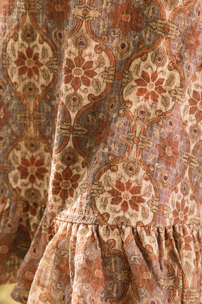 A close-up of textured fabric showcases an intricate floral and geometric pattern in warm orange, beige, and brown tones, accented by gathered ruffles at the hem—perfect for the Ivy City Co Teen Draper Dress in Golden Hour Tesserae, known for its elegant balloon sleeves.